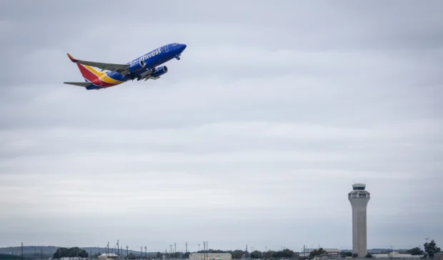 A Southwest Airlines plane takes off from Austin-Bergstrom International Airport, with the airport control tower visible in the background under a cloudy sky.